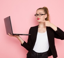 front-view-of-female-office-worker-in-black-strict-jacket-holding-using-laptop-on-light-pink-wall