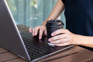 womans-hands-with-paper-cup-of-coffee-or-tea-and-laptop-in-cafe-or-home-terrace